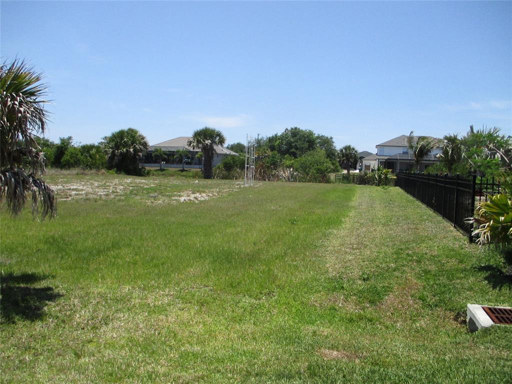 A grassy, vacant residential lot features a black metal fence along the right side — 14478 LILLIAN CIRCLE, PORT CHARLOTTE, FL