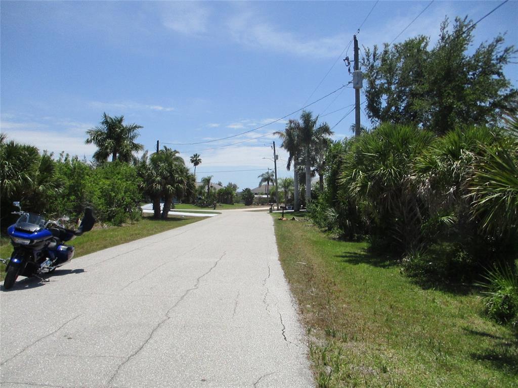 A paved road leads through a residential area with palm trees and a parked motorcycle — 14478 LILLIAN CIRCLE, PORT CHARLOTTE, FL