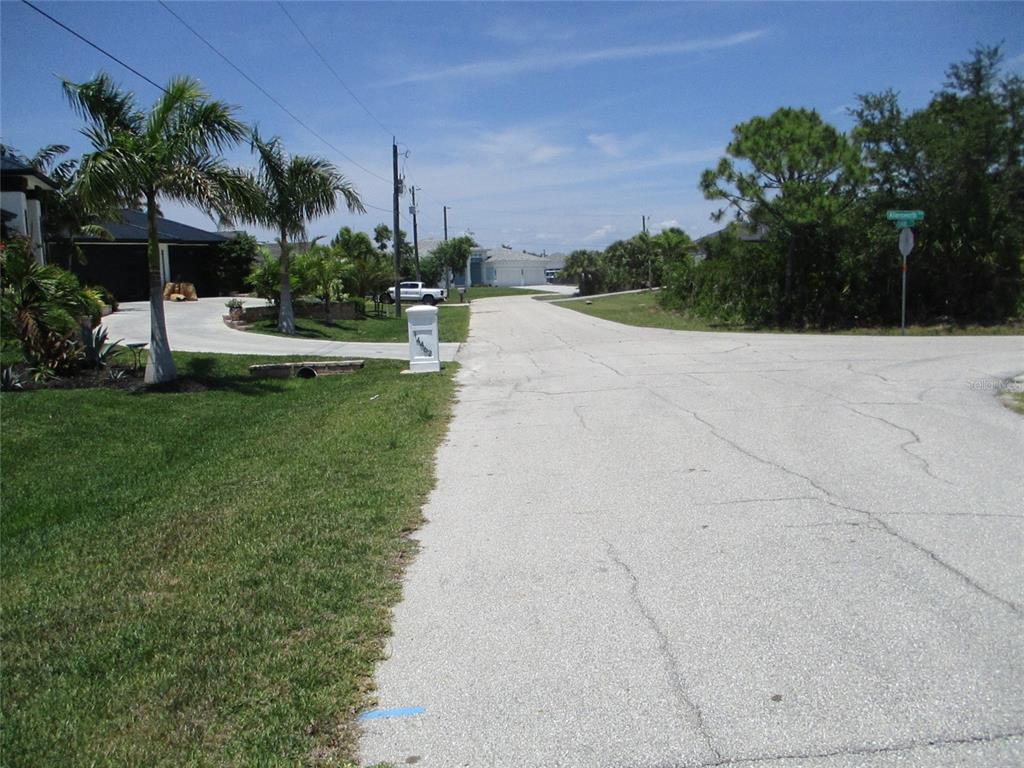 A paved residential street leads toward houses surrounded by palm trees and lush vegetation — 14478 LILLIAN CIRCLE, PORT CHARLOTTE, FL