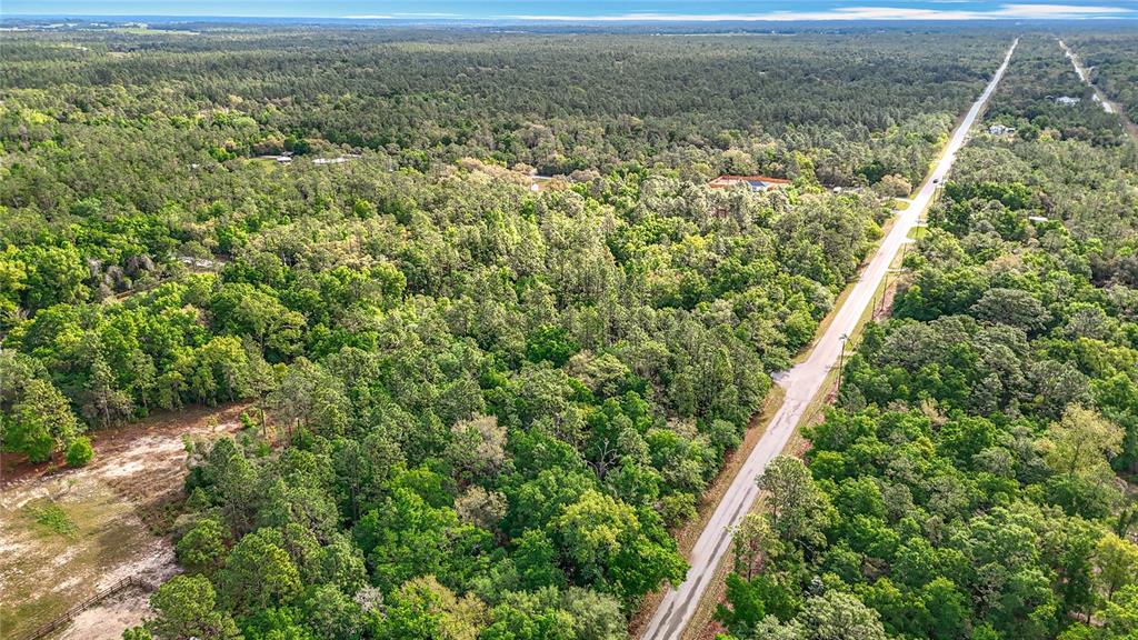 An aerial view shows a paved road running through a dense, wooded rural landscape — 0 SW BREEZY POINT DRIVE, DUNNELLON, FL