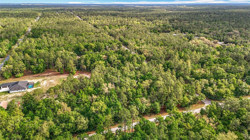 An aerial view shows a residential lot surrounded by dense forest with a nearby house — 0 SW BREEZY POINT DRIVE, DUNNELLON, FL