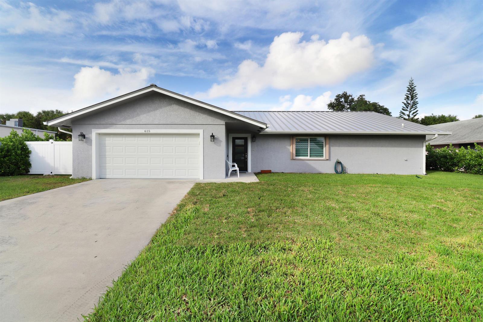 A single-story gray house with a metal roof, white garage door, and a front lawn — 615 NE 15th Place, Boynton Beach FL 33435, BOYNTON BEACH, FL