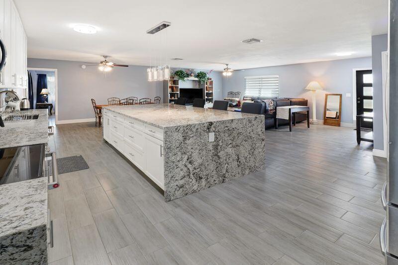 A spacious open-concept kitchen features a large granite-topped island, white cabinetry, and gray tile flooring — 615 NE 15th Place, Boynton Beach FL 33435, BOYNTON BEACH, FL