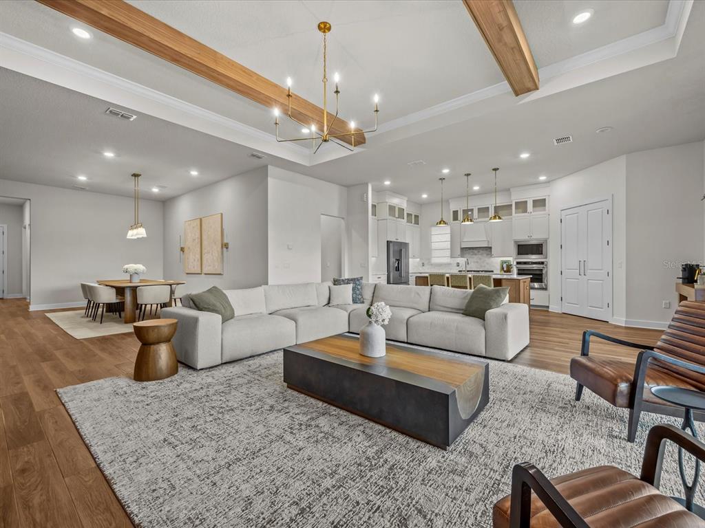 An open-concept living room features wood ceiling beams, a large sectional, and a modern kitchen — 15326 WILLOW RIDGE DRIVE, MONTVERDE, FL