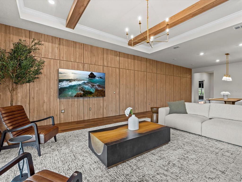 A living room features a wood-paneled accent wall, a mounted television, and a modern chandelier — 15326 WILLOW RIDGE DRIVE, MONTVERDE, FL