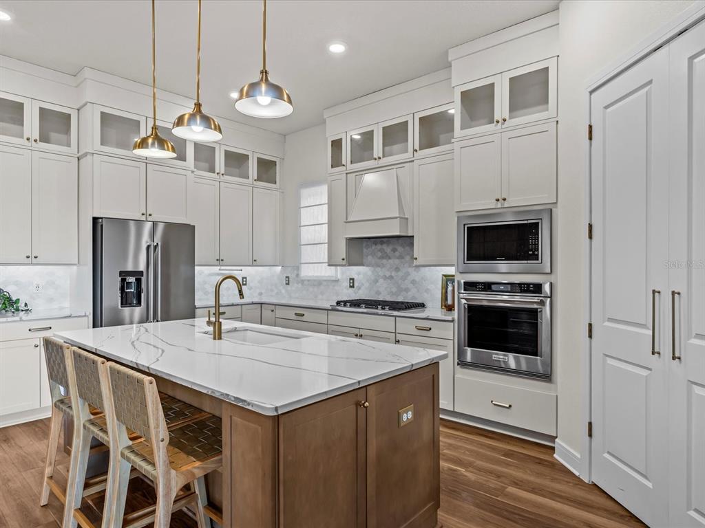 A modern kitchen features white cabinetry, a wood-toned island with marble countertops, and stainless appliances — 15326 WILLOW RIDGE DRIVE, MONTVERDE, FL