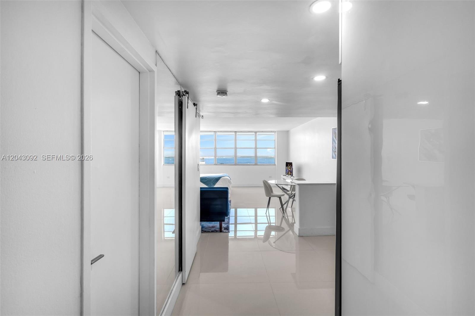 A bright, minimalist room features white tile floors, a sliding barn door, and ocean views — 801 Brickell Bay Dr # 669, Miami FL 33131, MIAMI, FL