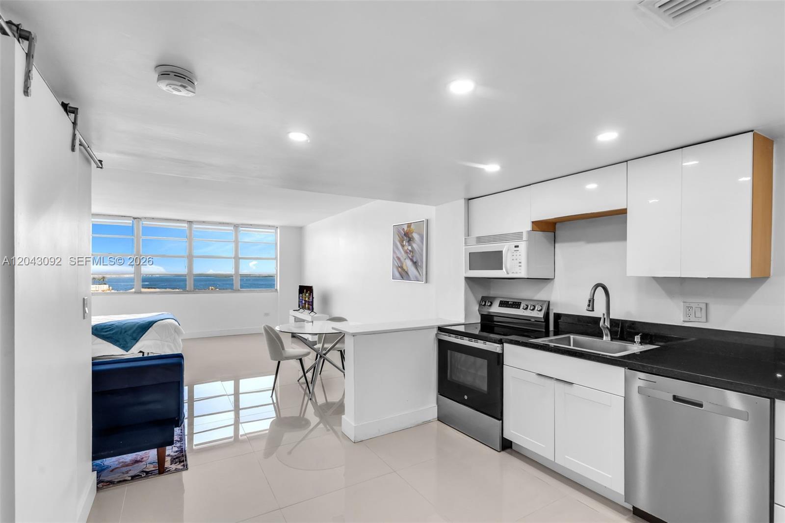 A modern kitchen with white cabinets and black countertops overlooks a bedroom and ocean view — 801 Brickell Bay Dr # 669, Miami FL 33131, MIAMI, FL