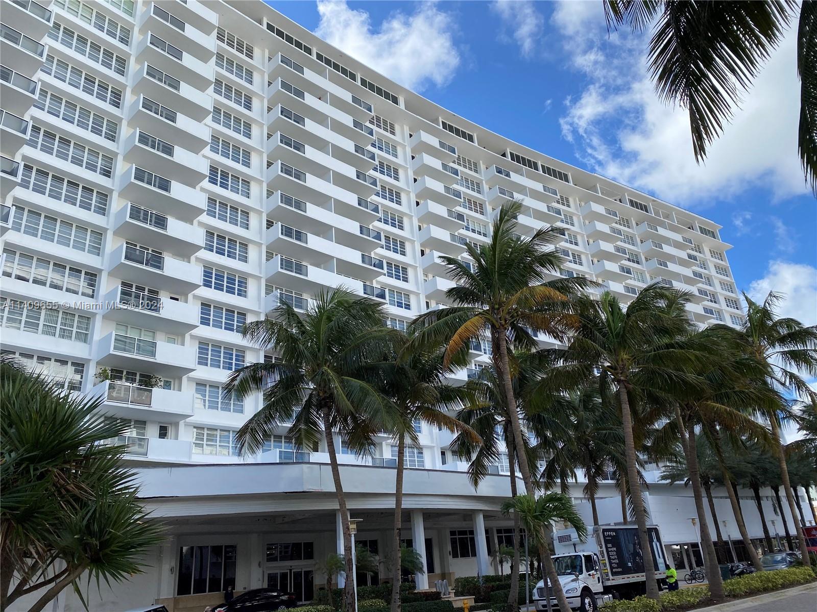 A tall white residential building with balconies stands behind a row of palm trees — 100 Lincoln Rd # 939, Miami Beach FL 33139, MIAMI BEACH, FL