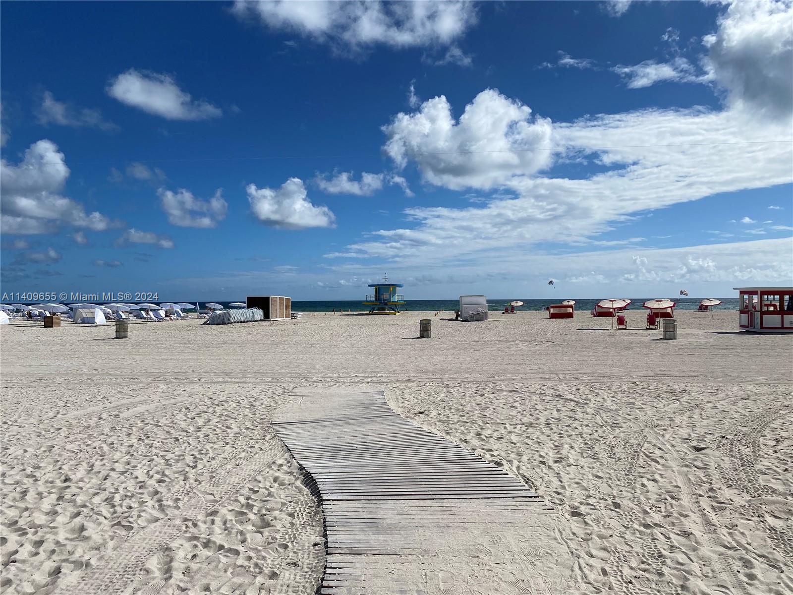 A wooden walkway leads across a sandy beach toward the ocean under a blue sky — 100 Lincoln Rd # 939, Miami Beach FL 33139, MIAMI BEACH, FL