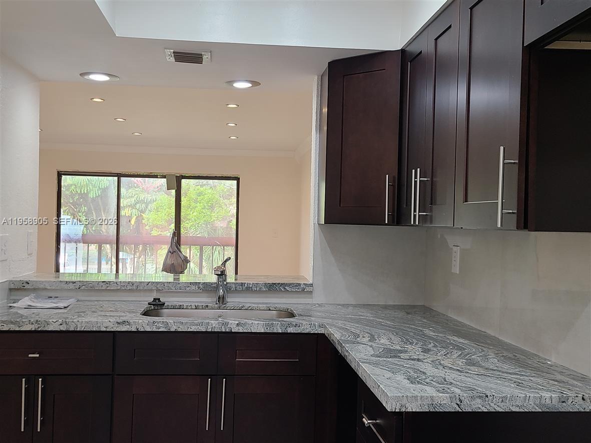 A kitchen features dark wood cabinets, granite countertops, a stainless steel sink, and a pass-through window — 4020 Del Rio Way, Sunrise FL 33351, SUNRISE, FL