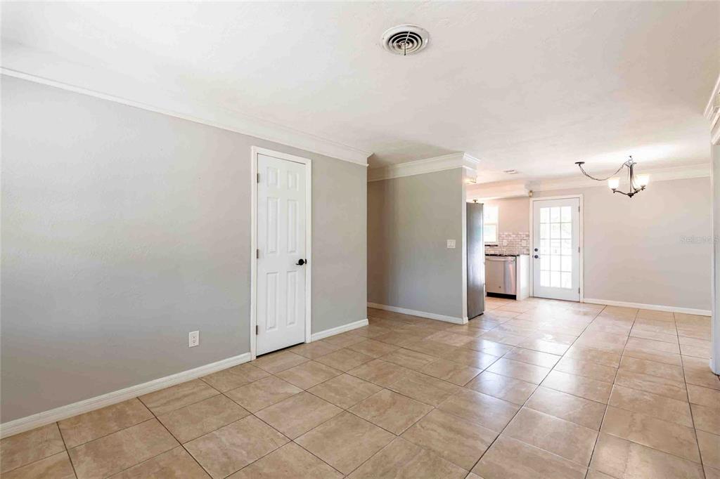 A room with light gray walls, beige tile flooring, a white door, and a kitchen view — 2741 37TH STREET S, ST PETERSBURG, FL
