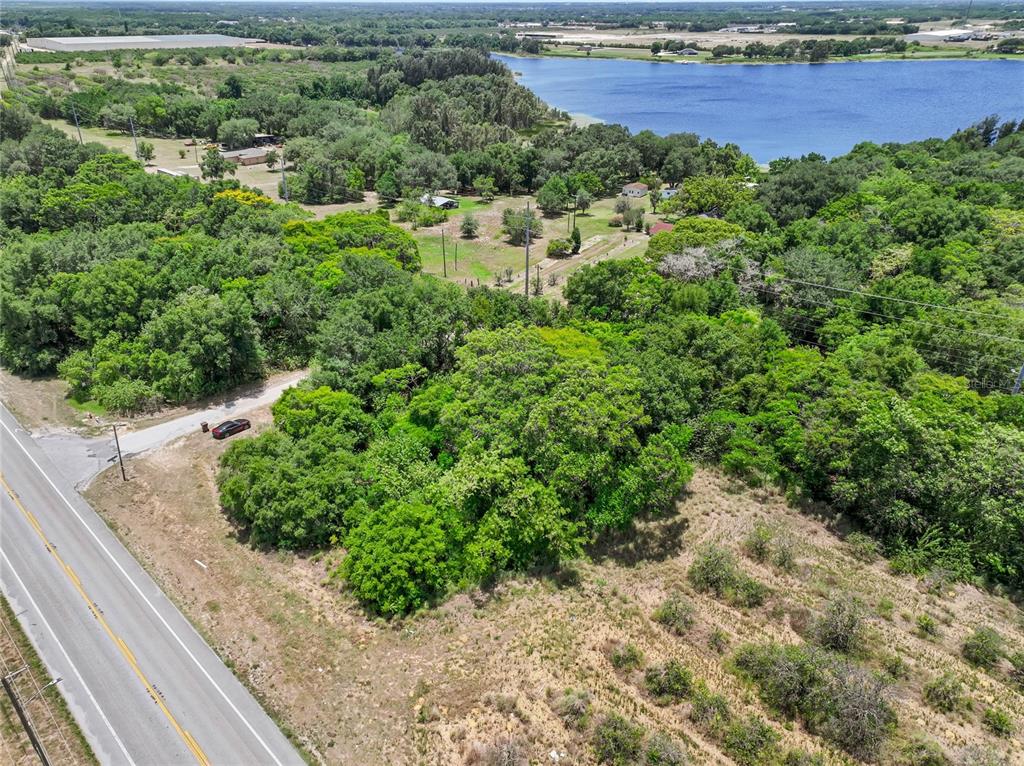 An aerial view shows a wooded lot bordering a lake next to a paved road — SR-17, HAINES CITY, FL