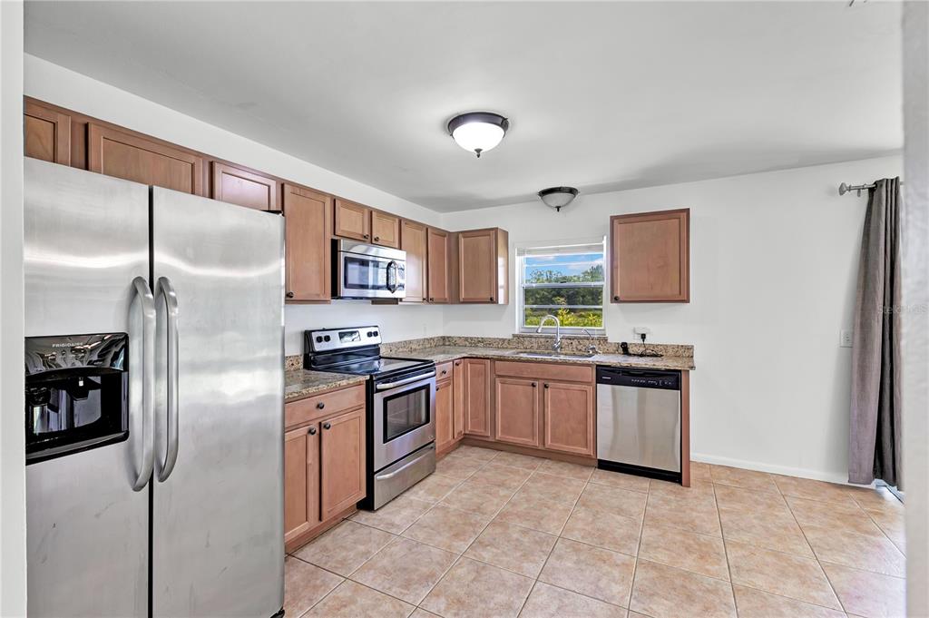 A kitchen with wood cabinets, stainless steel appliances, granite countertops, and tile flooring — 2445 OLD HICKORY TREE ROAD, ST CLOUD, FL