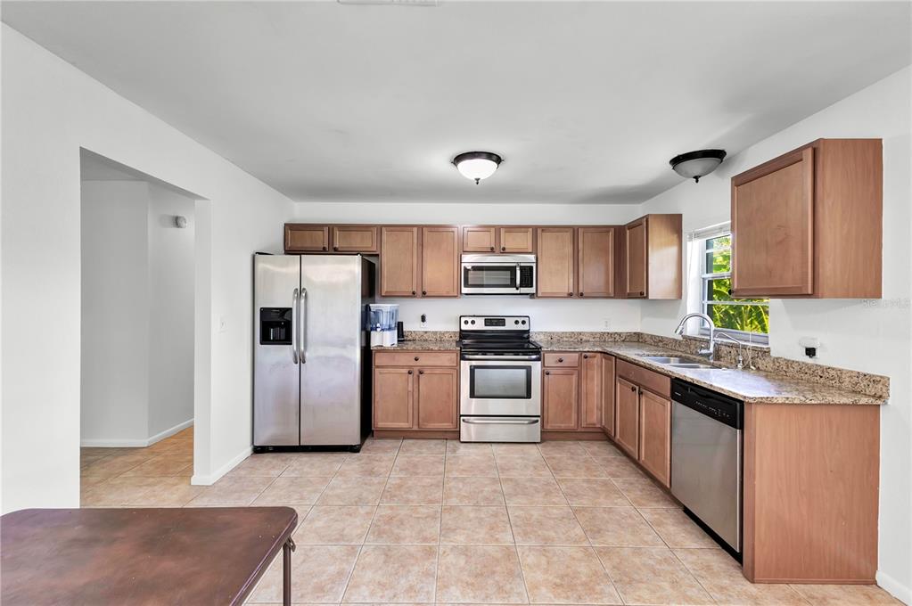 A kitchen features wood cabinets, stainless steel appliances, granite countertops, and light-colored tile flooring — 2445 OLD HICKORY TREE ROAD, ST CLOUD, FL