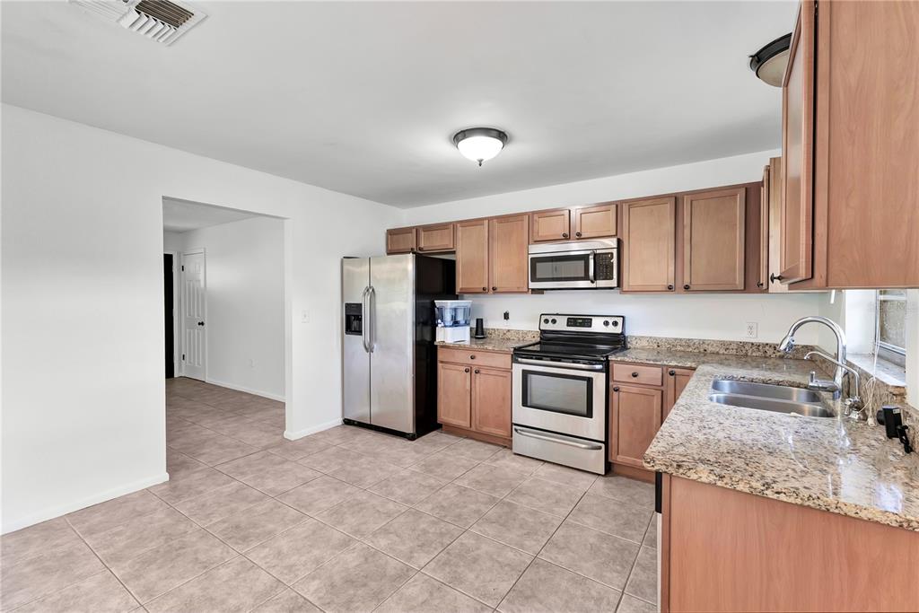 A kitchen with light wood cabinets, granite countertops, stainless steel appliances, and tiled flooring — 2445 OLD HICKORY TREE ROAD, ST CLOUD, FL