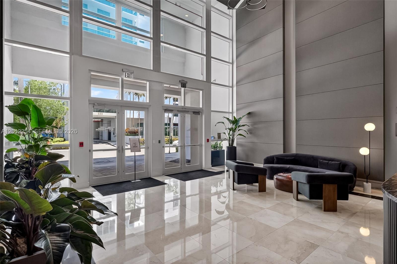 A modern building lobby features floor-to-ceiling windows, marble tile flooring, and contemporary lounge seating — 350 NE 24th St # 609, Miami FL 33137, MIAMI, FL