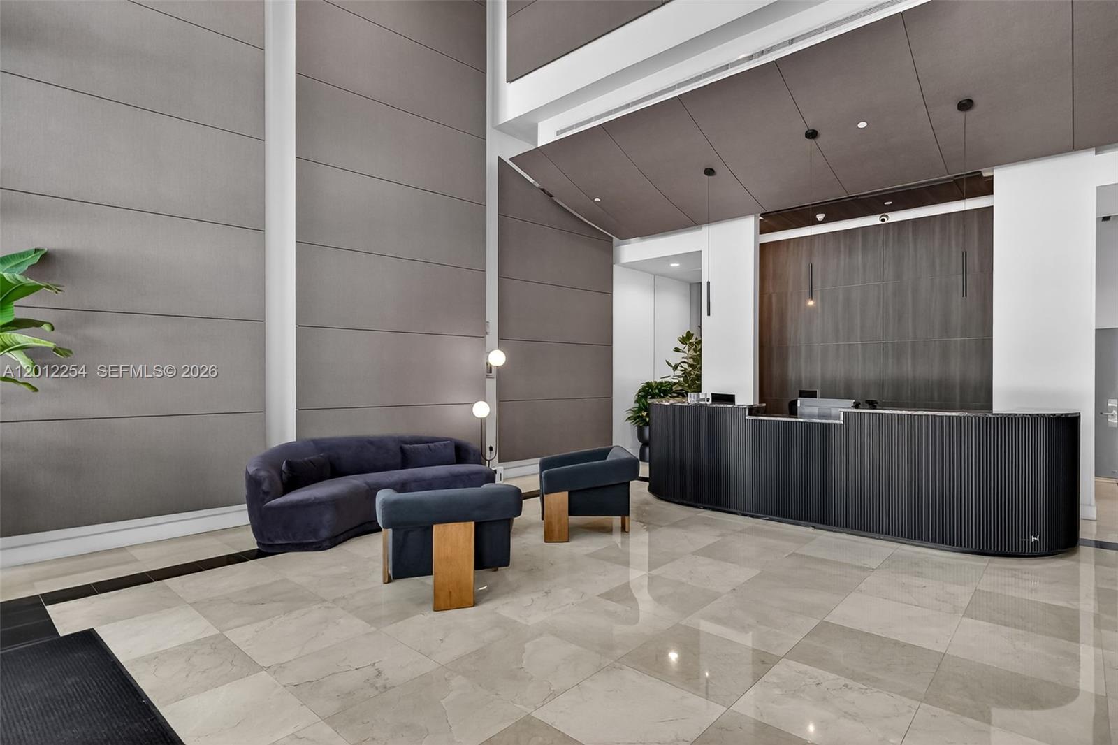 A modern lobby features a curved reception desk, plush seating, and large-format tile flooring — 350 NE 24th St # 609, Miami FL 33137, MIAMI, FL