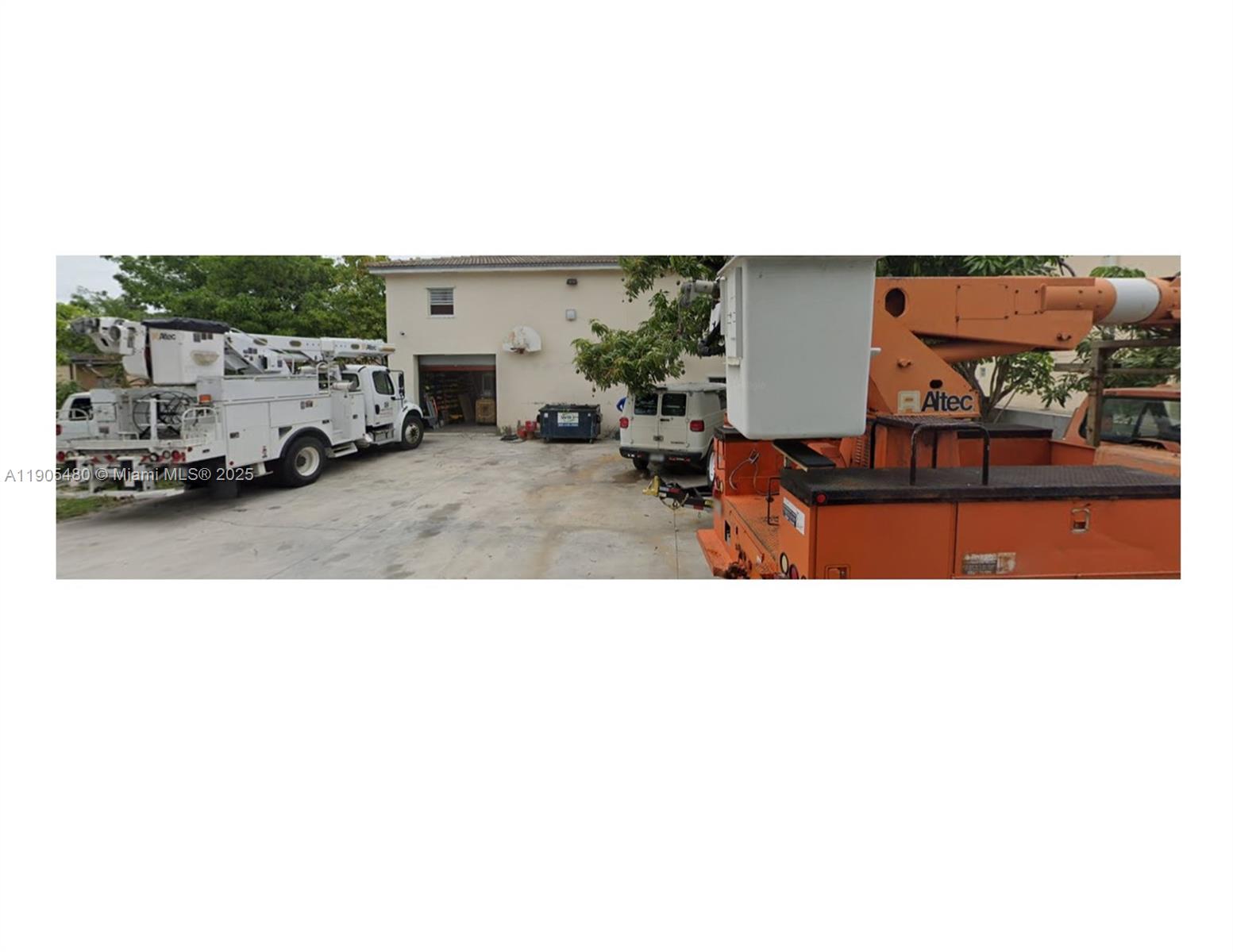 A concrete lot features a building with a garage door and several utility bucket trucks — 660 Miller Dr, Miami Springs FL 33166, MIAMI SPRINGS, FL