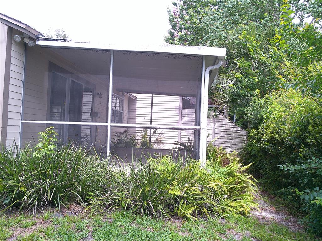 A screened-in patio with a metal roof sits beside a house surrounded by lush landscaping — 1387 DUNHILL DRIVE, LONGWOOD, FL