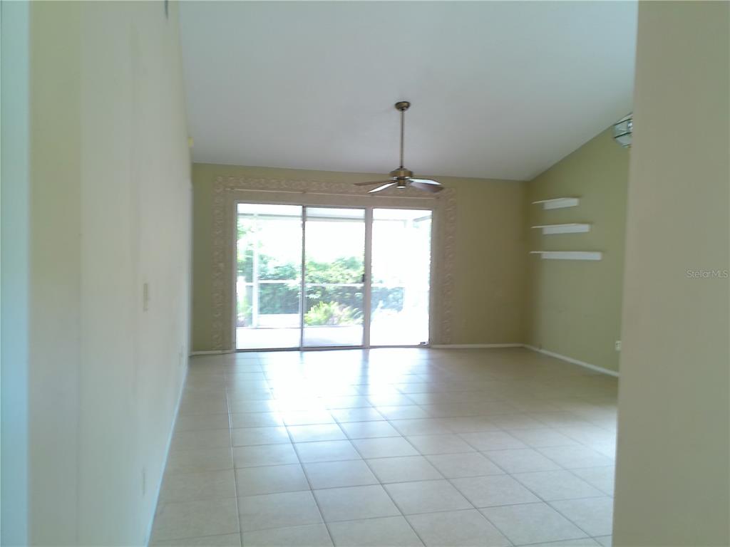 A living room with light-colored tile flooring, a vaulted ceiling, and sliding glass patio doors — 1387 DUNHILL DRIVE, LONGWOOD, FL