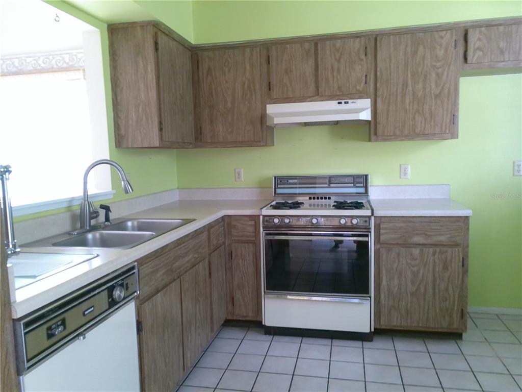 A kitchen features wood-grain cabinets, white laminate countertops, a white stove, and light green walls — 1387 DUNHILL DRIVE, LONGWOOD, FL
