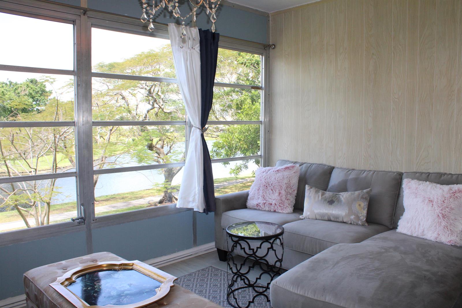 A living room features a gray sectional sofa, a glass-topped side table, and large windows — 14671 Bonaire Boulevard # 305, Delray Beach FL 33446, DELRAY BEACH, FL