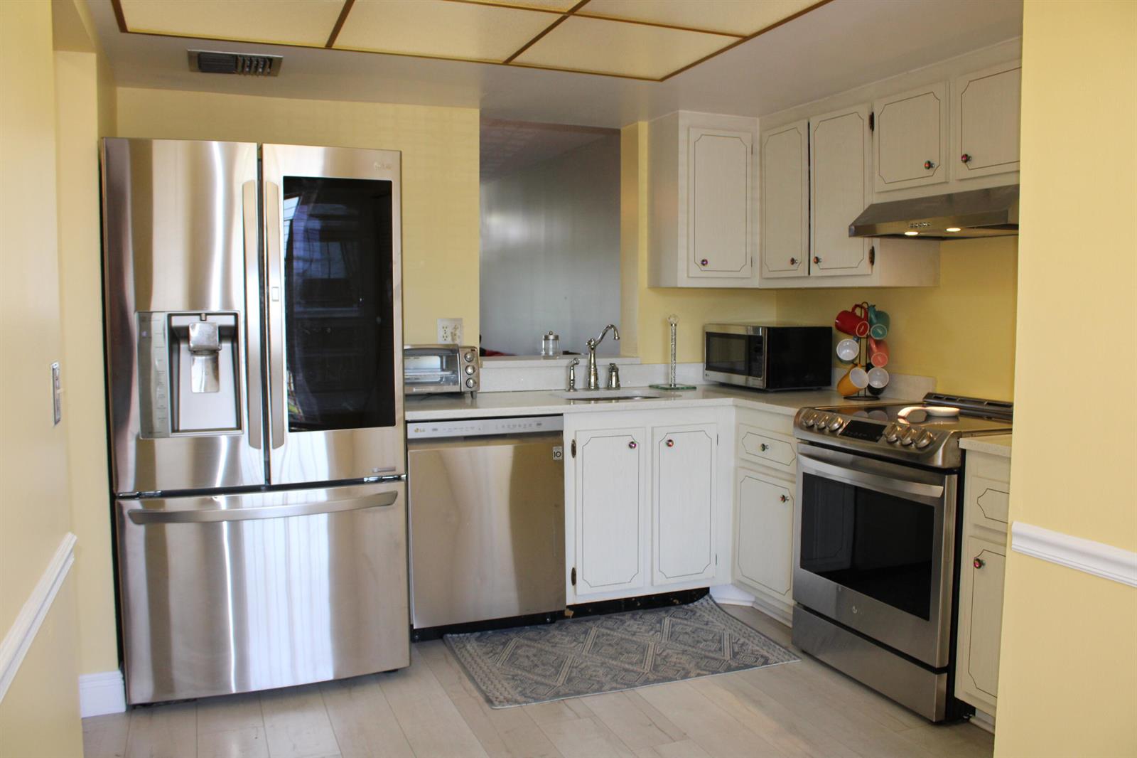 A kitchen with yellow walls, white cabinets, stainless steel appliances, and a light-colored floor — 14671 Bonaire Boulevard # 305, Delray Beach FL 33446, DELRAY BEACH, FL