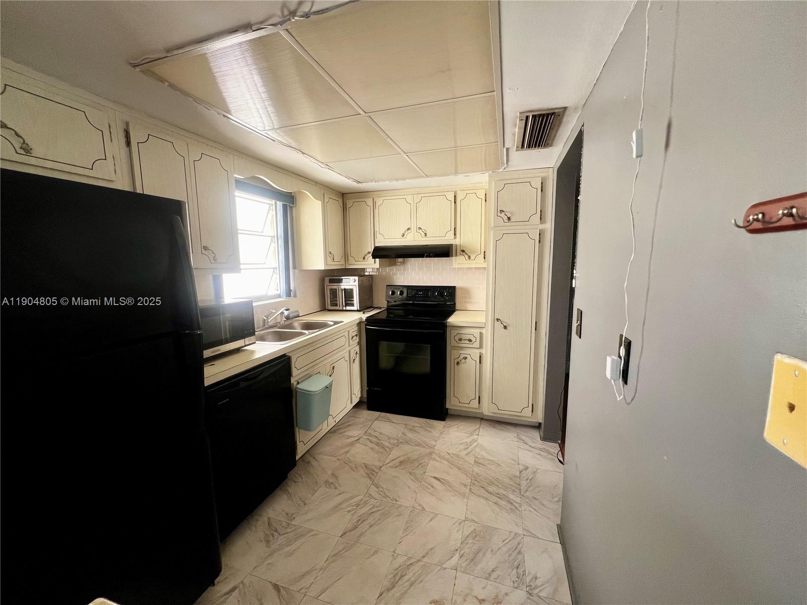 A kitchen features white cabinets, black appliances, and light-colored marble-patterned tile flooring — 1501 Arthur St # 7, Hollywood FL 33020, HOLLYWOOD, FL