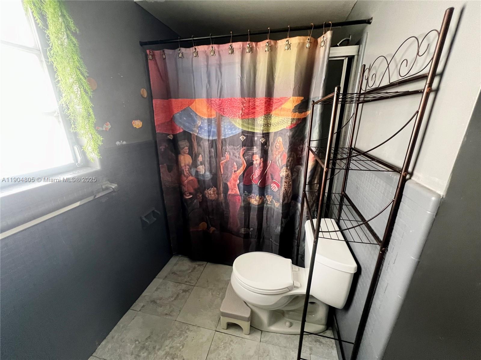 A bathroom features a patterned shower curtain, a toilet with a step stool, and shelving — 1501 Arthur St # 7, Hollywood FL 33020, HOLLYWOOD, FL