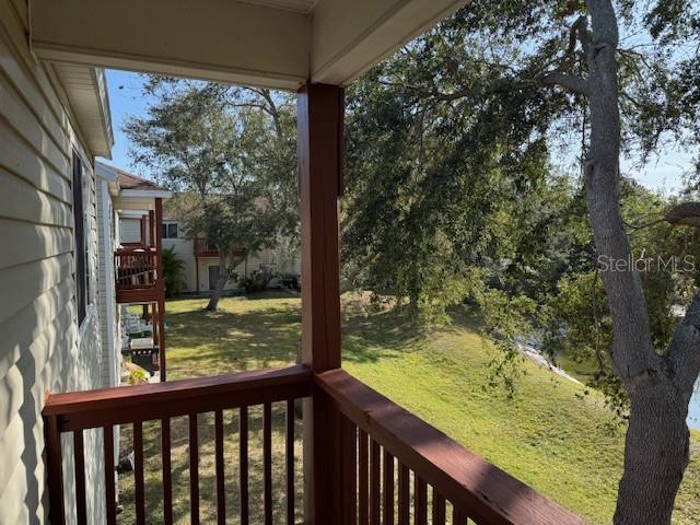 A view from a wooden balcony overlooking a grassy yard, trees, and a nearby building — 6740 MOONGLOW DRIVE UNIT 201, PORT RICHEY, FL