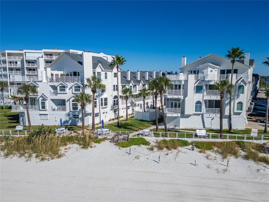 A multi-story white residential building sits directly behind a sandy beach with palm trees — 17960 GULF BLVD UNIT 108, REDINGTON SHORES, FL