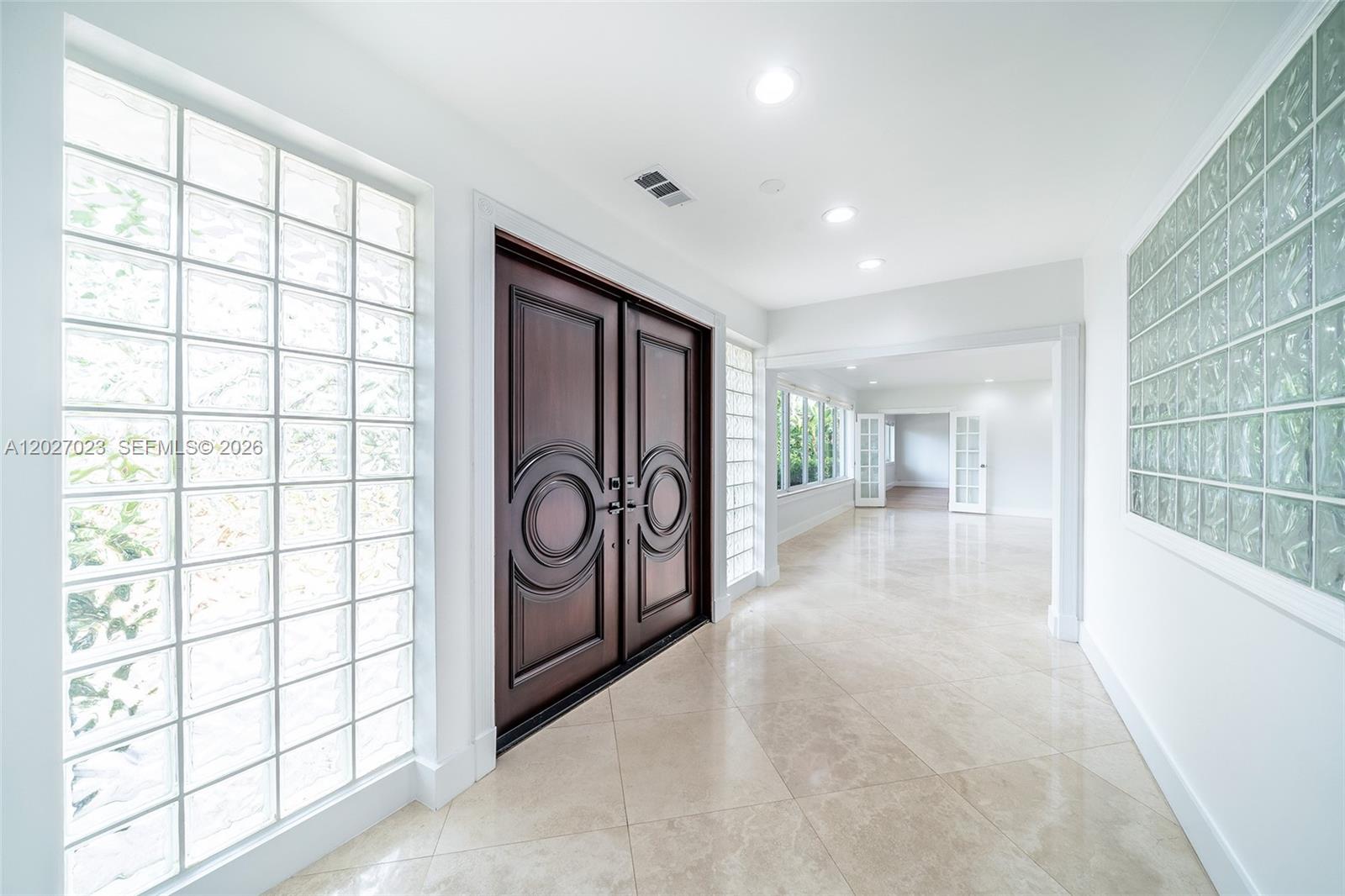 A bright entryway features a dark wood double door, glass block walls, and tile flooring — 9835 W Broadview Dr, Bay Harbor Islands FL 33154, BAY HARBOR ISLANDS, FL