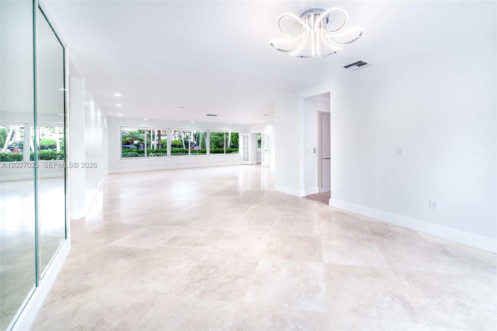 A bright, open-concept living area features large windows, light tile flooring, and a modern chandelier — 9835 W Broadview Dr, Bay Harbor Islands FL 33154, BAY HARBOR ISLANDS, FL