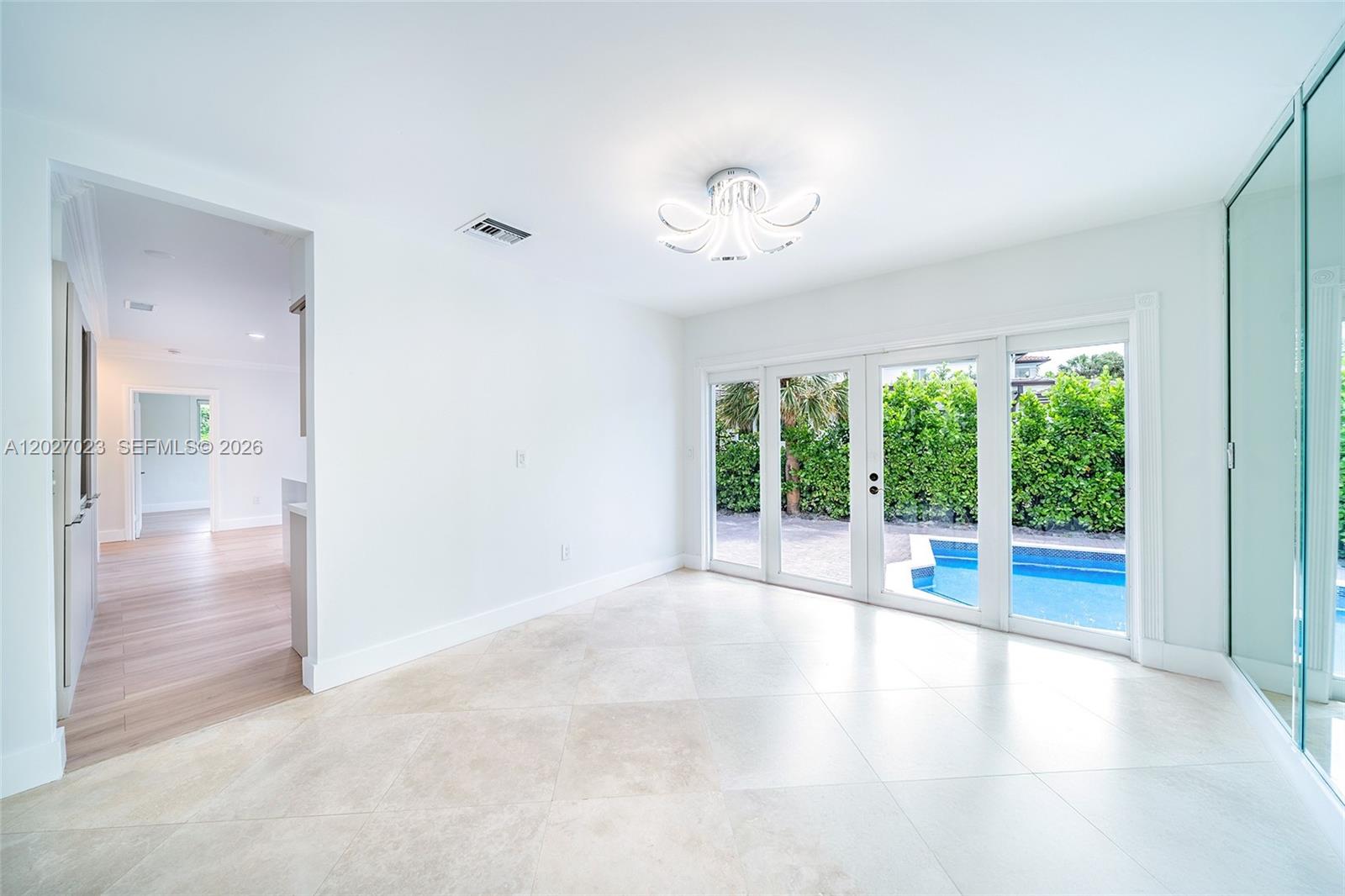 A bright room with light tile floors features a modern chandelier and sliding glass doors — 9835 W Broadview Dr, Bay Harbor Islands FL 33154, BAY HARBOR ISLANDS, FL
