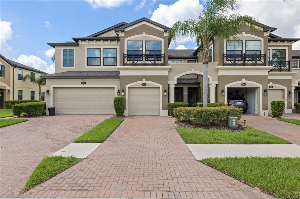 A multi-unit residential building with beige stucco, brick paver driveways, and attached garages — 18876 BEAUTYBERRY COURT, LUTZ, FL