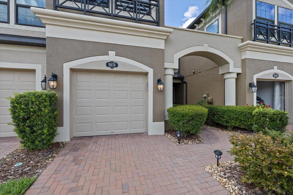 The exterior of a multi-story townhouse features a beige garage, brick driveway, and manicured landscaping — 18876 BEAUTYBERRY COURT, LUTZ, FL