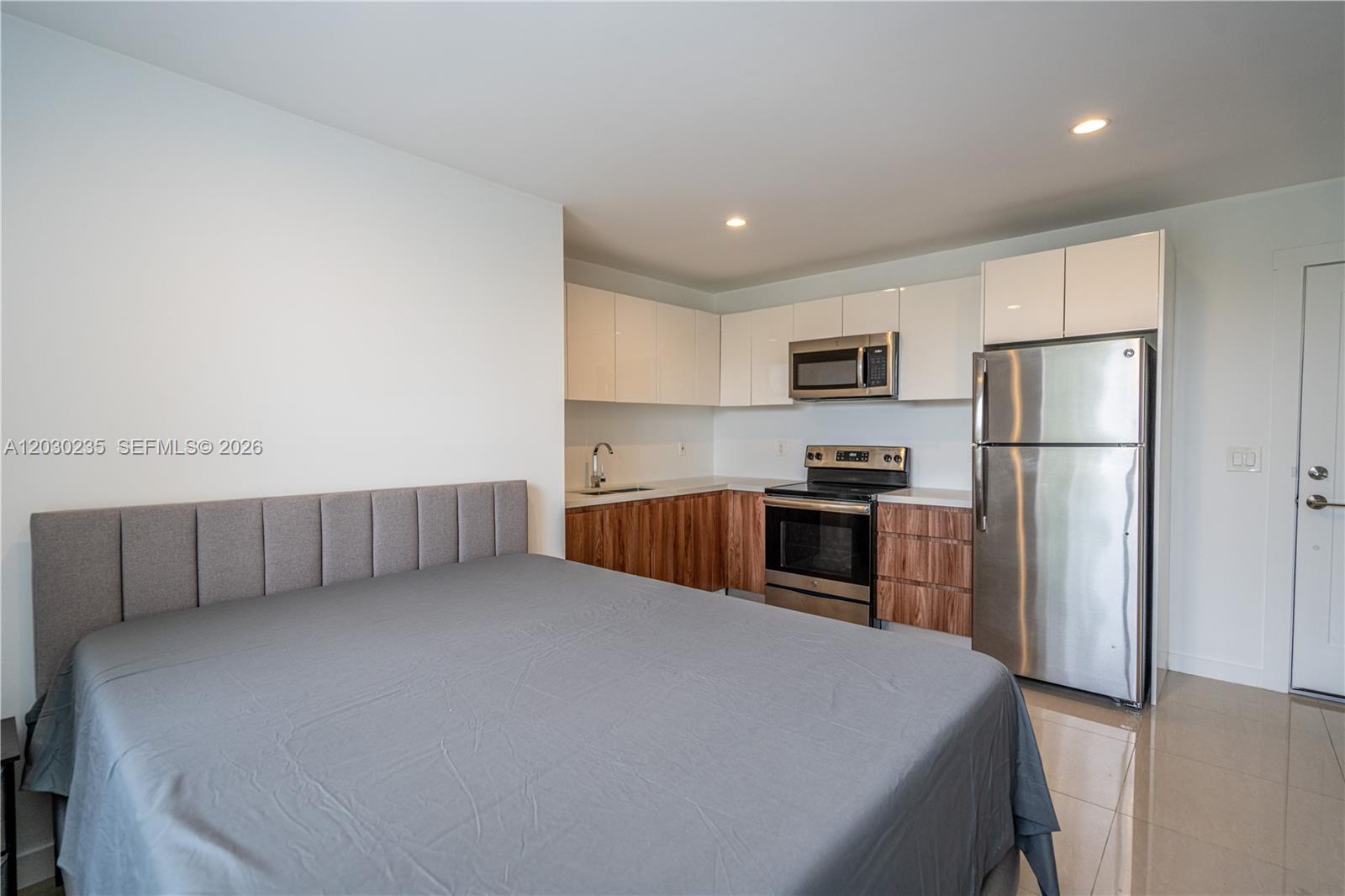 A studio apartment features a bed next to a kitchen with wood-grain cabinets — 924 Marseille Dr # 26, Miami Beach FL 33141, MIAMI BEACH, FL