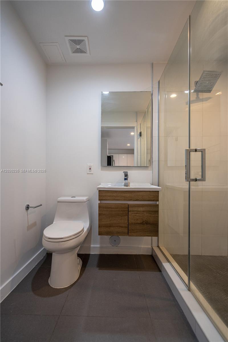 A modern bathroom features a white toilet, a wood-toned vanity, and a glass-enclosed shower — 924 Marseille Dr # 26, Miami Beach FL 33141, MIAMI BEACH, FL