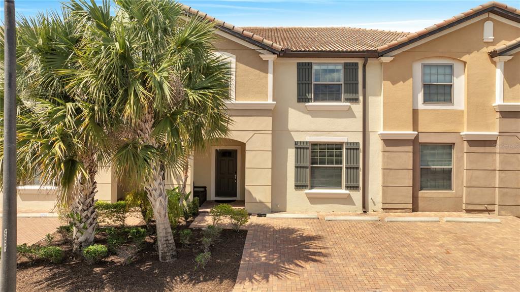 A two-story townhouse exterior features a brick driveway, a palm tree, and a front entrance — 8827 GENEVE COURT, KISSIMMEE, FL