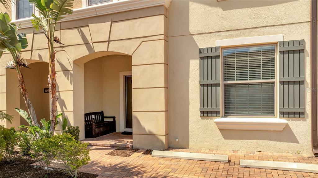 The exterior of a beige stucco building features a covered entryway with a wooden bench — 8827 GENEVE COURT, KISSIMMEE, FL