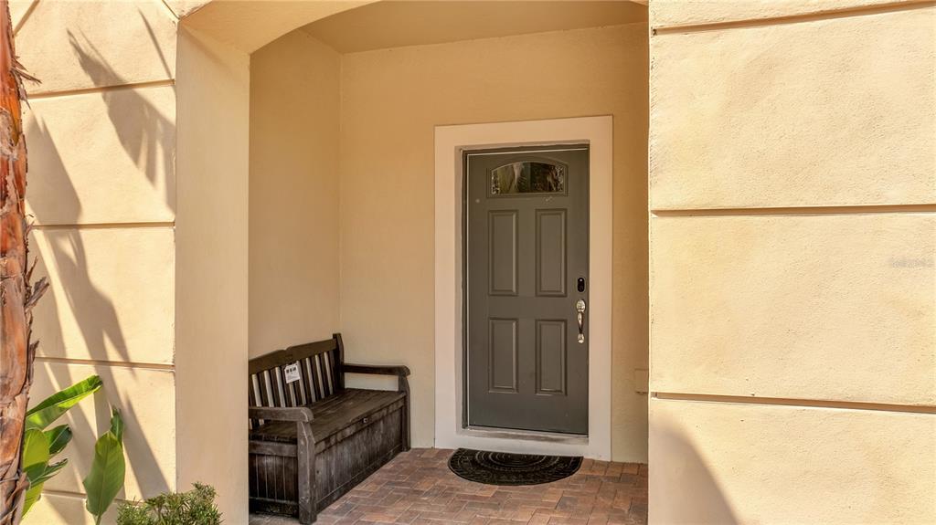 A dark gray front door with a bench sits on a paved porch entryway — 8827 GENEVE COURT, KISSIMMEE, FL
