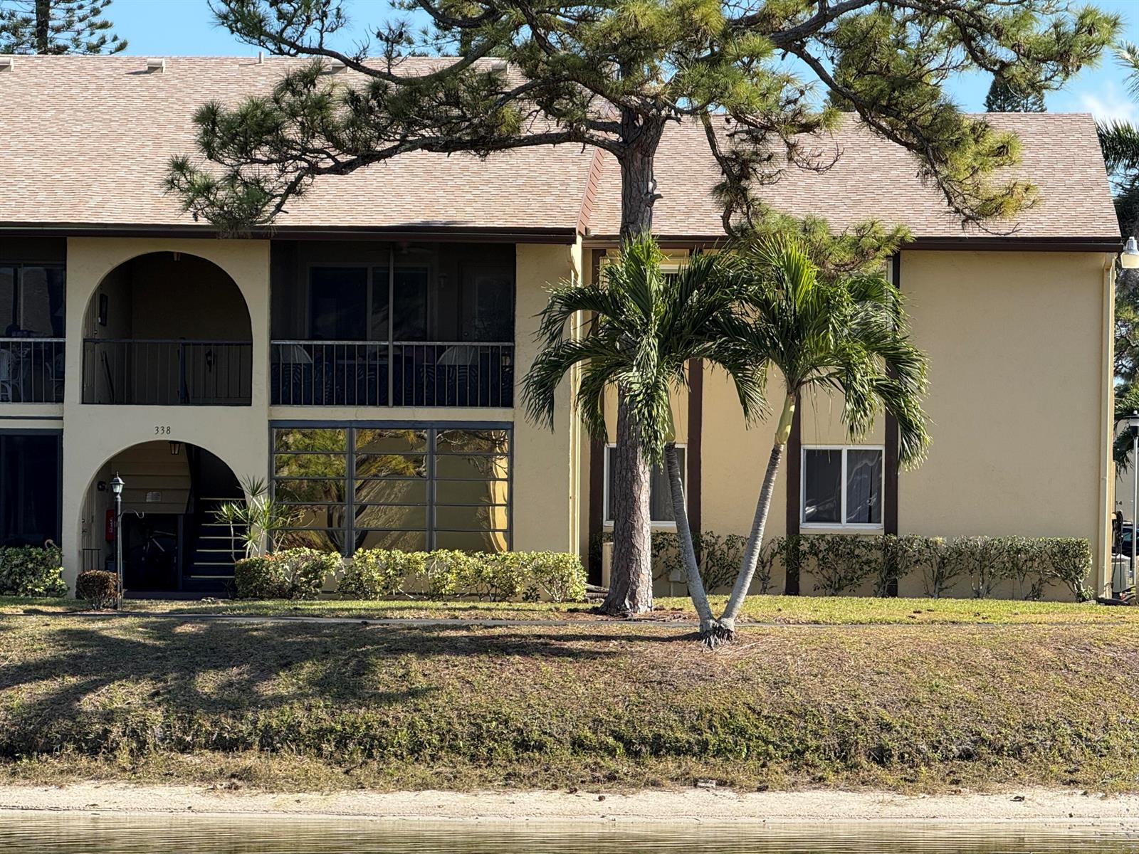 A two-story apartment building with a screened balcony and palm trees sits near a pond — 338 Pine Ridge Circle # 2, FL 33463, FL