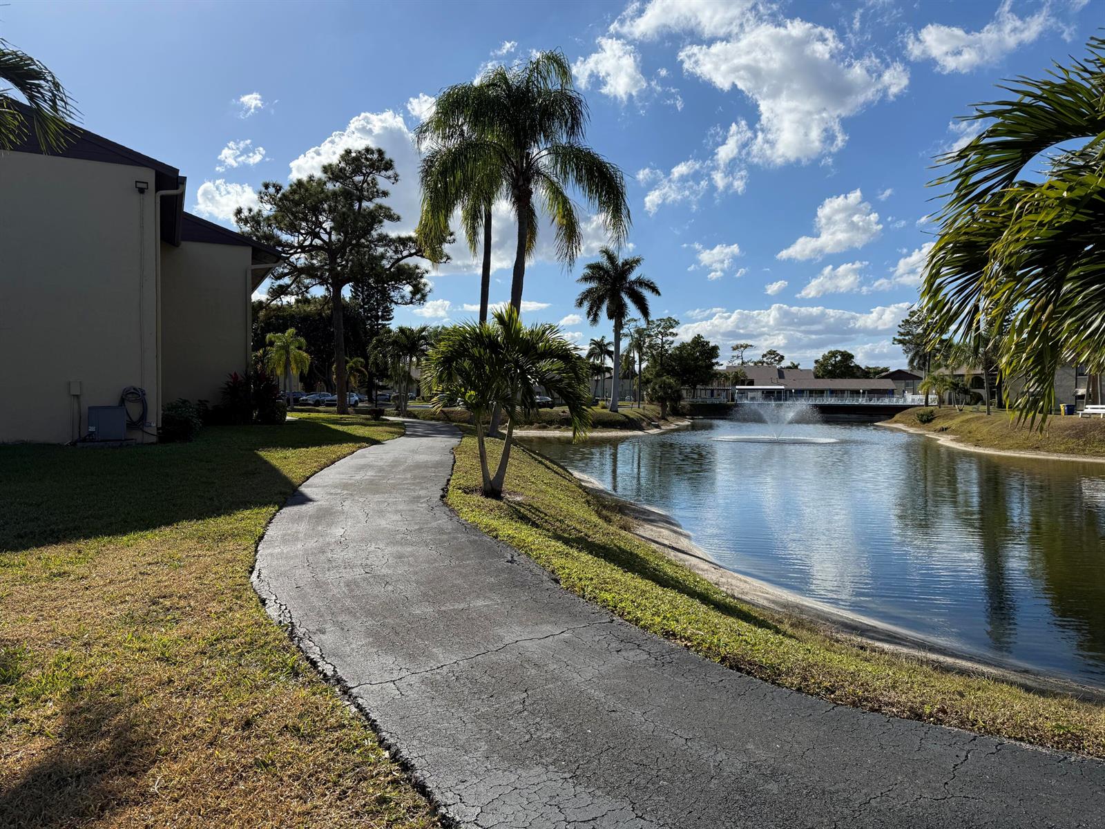 A paved walking path winds along a pond with a fountain near palm trees and buildings — 338 Pine Ridge Circle # 2, FL 33463, FL