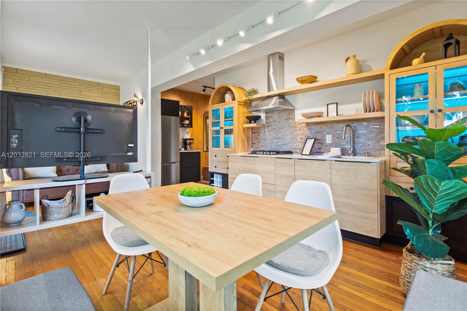 A dining area with a wooden table and white chairs sits before a modern kitchen — 499 NE 112th St, Miami FL 33161, MIAMI, FL