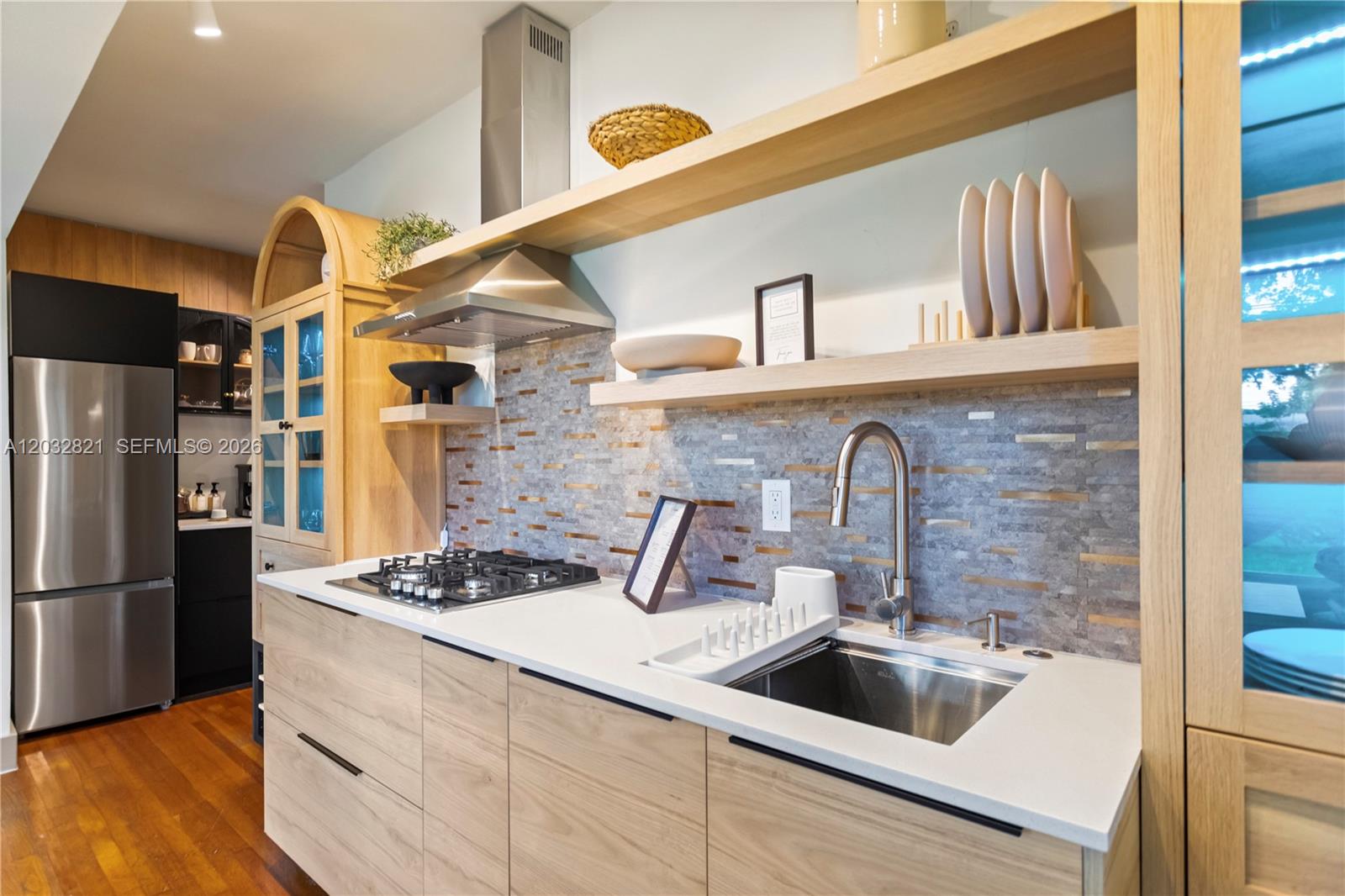 A modern kitchen features light wood cabinets, a stone tile backsplash, and stainless steel appliances — 499 NE 112th St, Miami FL 33161, MIAMI, FL
