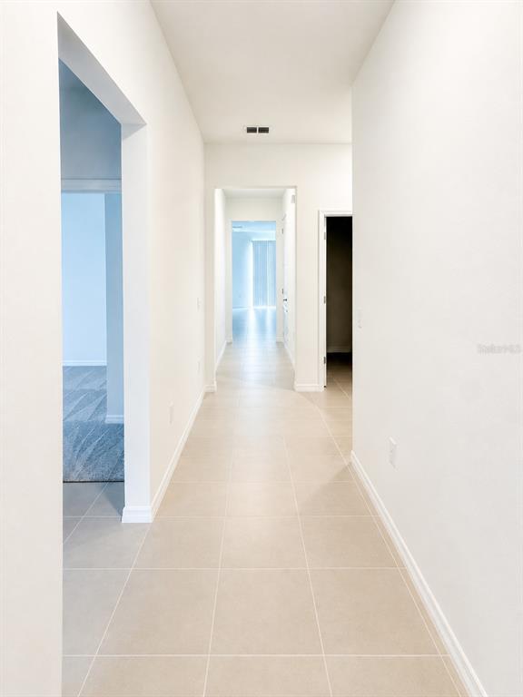 A long hallway with light-colored tile flooring and white walls leads to a bright room — 333 MARION LOOP, HAINES CITY, FL