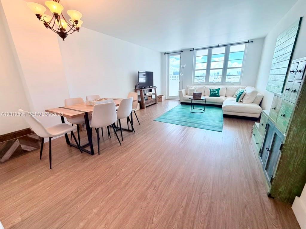 An open-concept living and dining area features light wood flooring, a sectional sofa, and windows — 100 Lincoln Rd # 922, Miami Beach FL 33139, MIAMI BEACH, FL