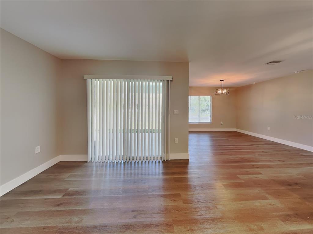 A living area with wood-look flooring, vertical blinds on a sliding door, and an adjacent room — 15476 CHAMBERLAIN BOULEVARD, PORT CHARLOTTE, FL