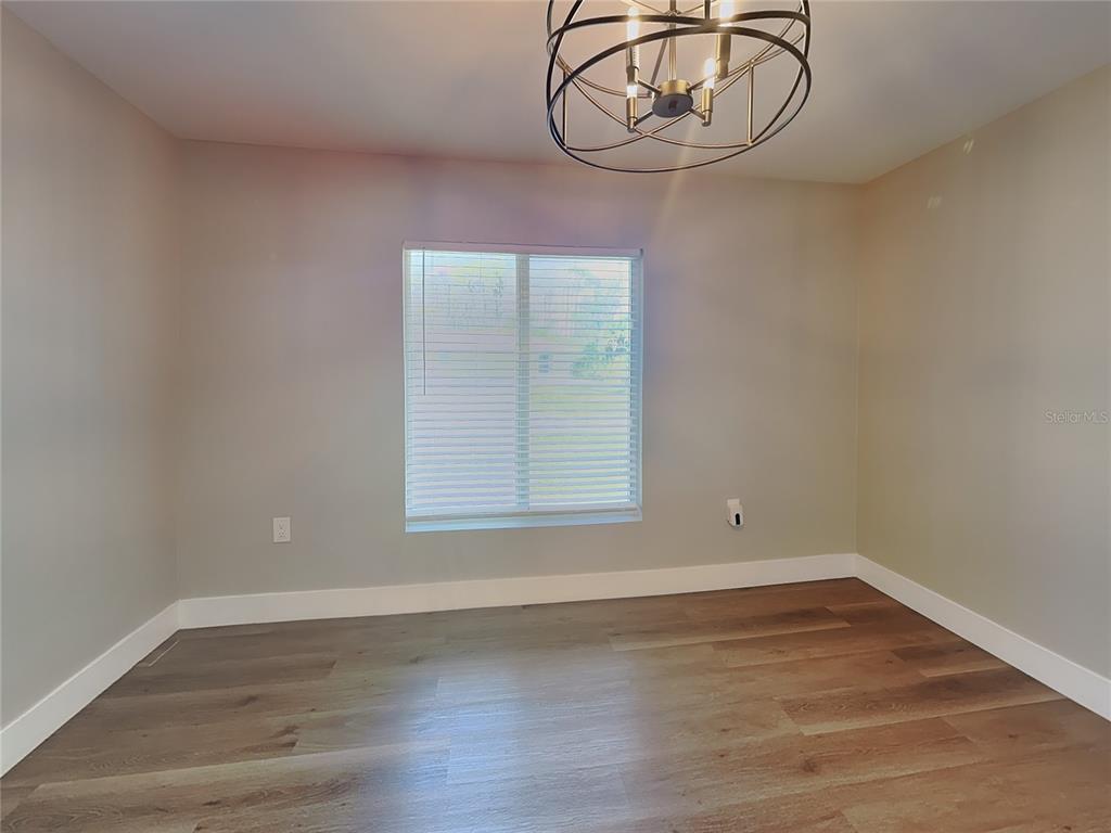 An empty room features light-colored walls, wood-look flooring, a window with blinds, and a chandelier — 15476 CHAMBERLAIN BOULEVARD, PORT CHARLOTTE, FL